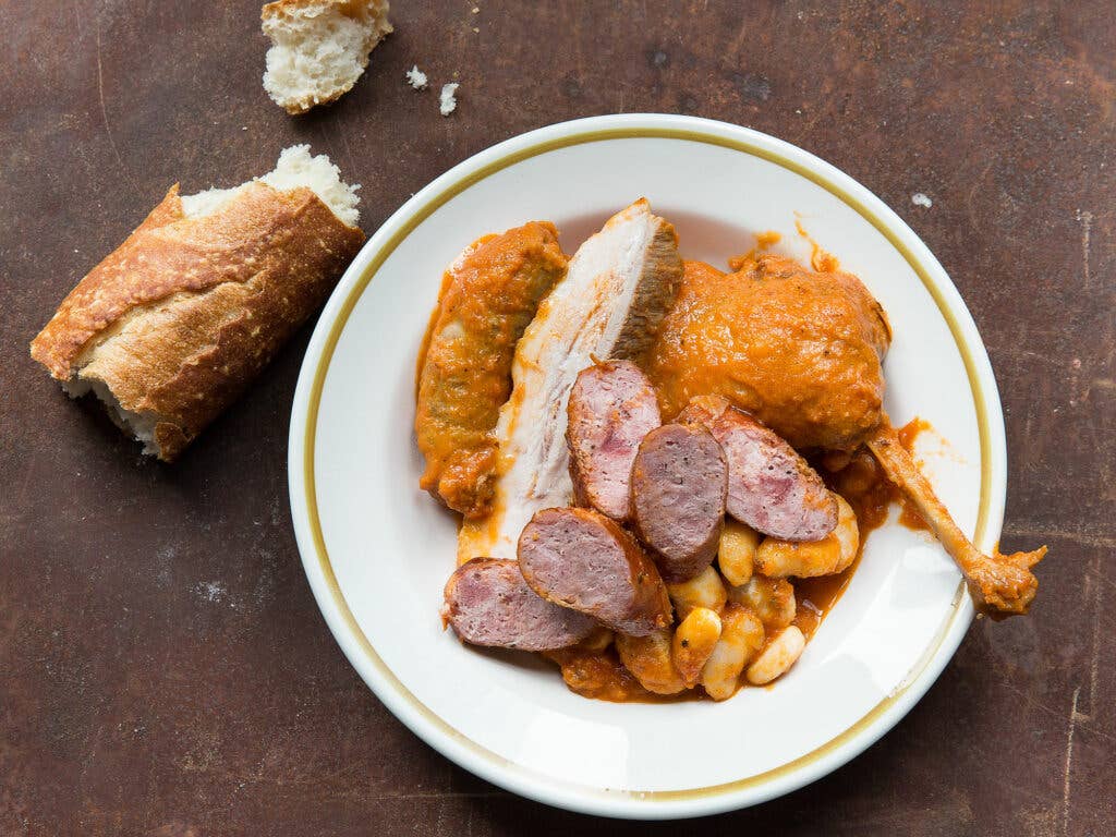 plate of duck leg confit with sausage and crusty bread