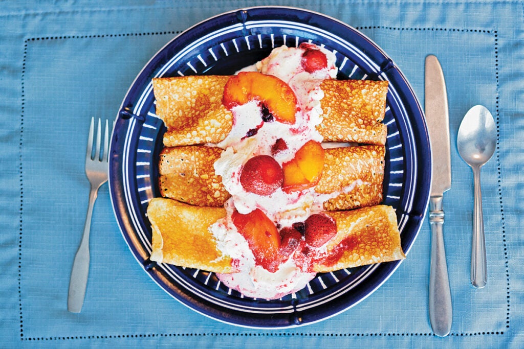 Crêpes stuffed with cheese and topped with stewed blueberries, strawberries, and peaches