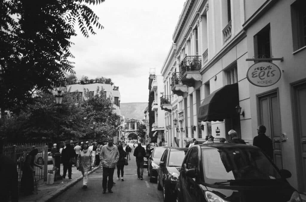 Pedestrians walk in the middle of the road from Monastiraki to the Arch of Hadrian. These areas are usually filled with tourists, and here you can see them taking in the area's beautiful buildings.