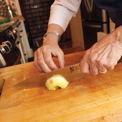 Working with one apple half at a time, she makes thin crosswise slices, keeping the heel of her knife slightly above the cutting board with each downstroke so the slices remain connected at one end