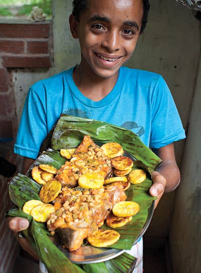A teen holds fish with shrimp sauce and fried plantains.