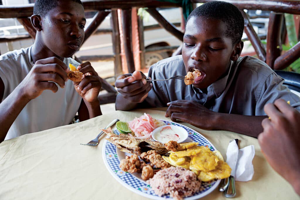 Boys enjoy a lunch of fried conch, kingfish, plantains, and rice and beans with coconut milk at Restaurante Corozal, in Corozal, Honduras