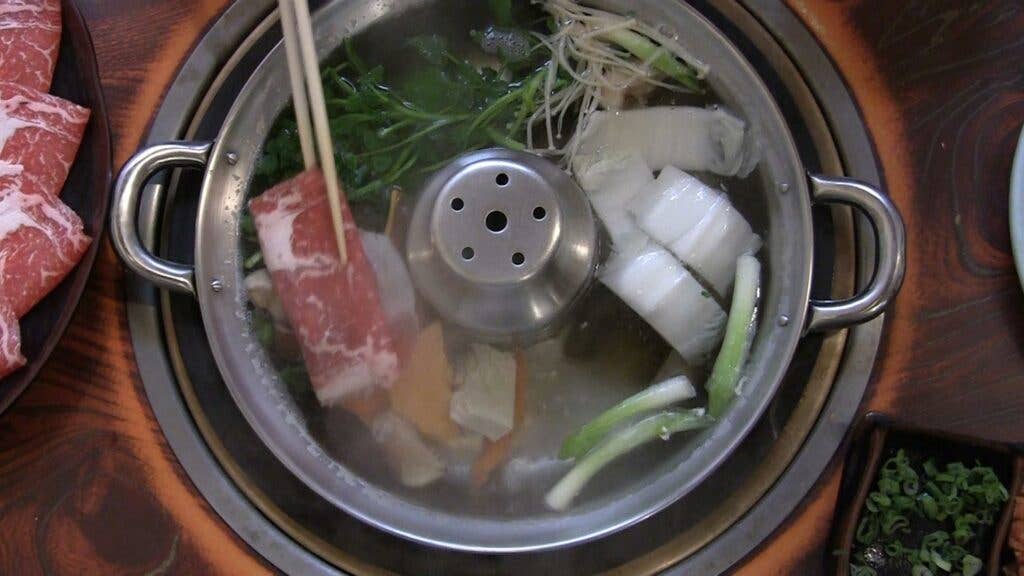 A piece of beef swishes through the hot water and vegetables.