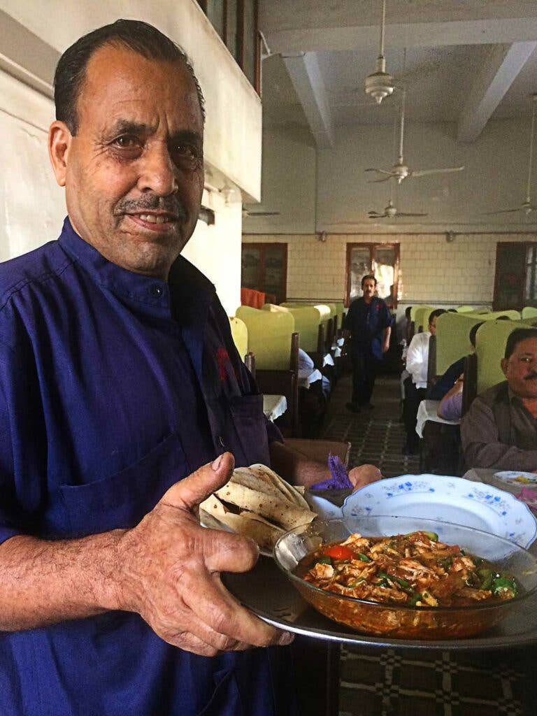 A server at Khairabad carries a platter of ginger chicken and roti.