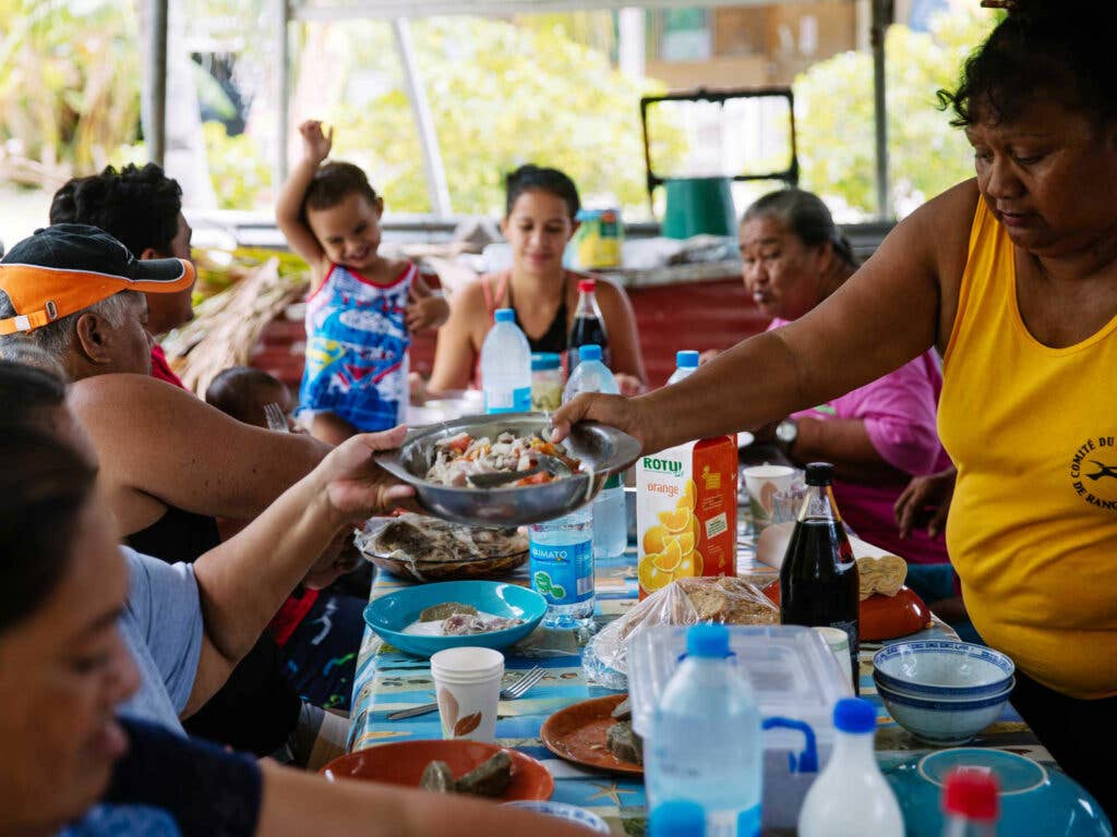 a Tahitian family passes dishes around a dinner table