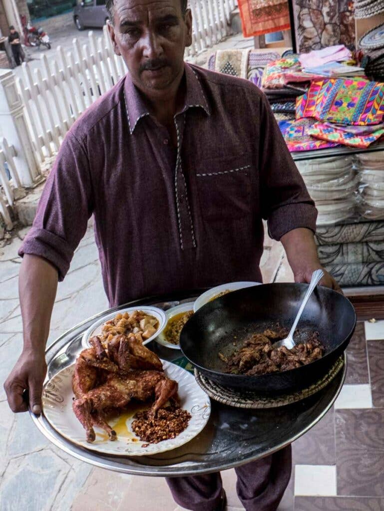 A server carries a plate of *patakha* chicken, served with additional chiles on the side.