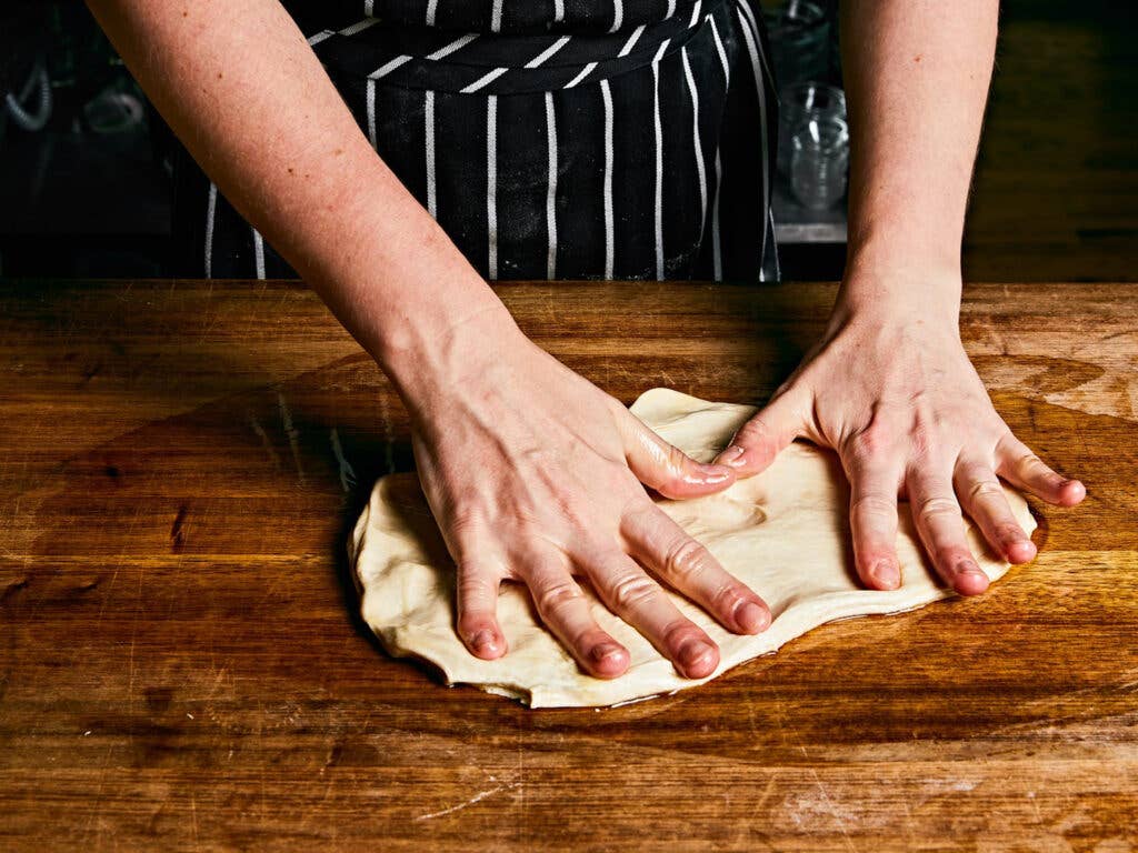 Spreading dough out by hand on an oiled board.