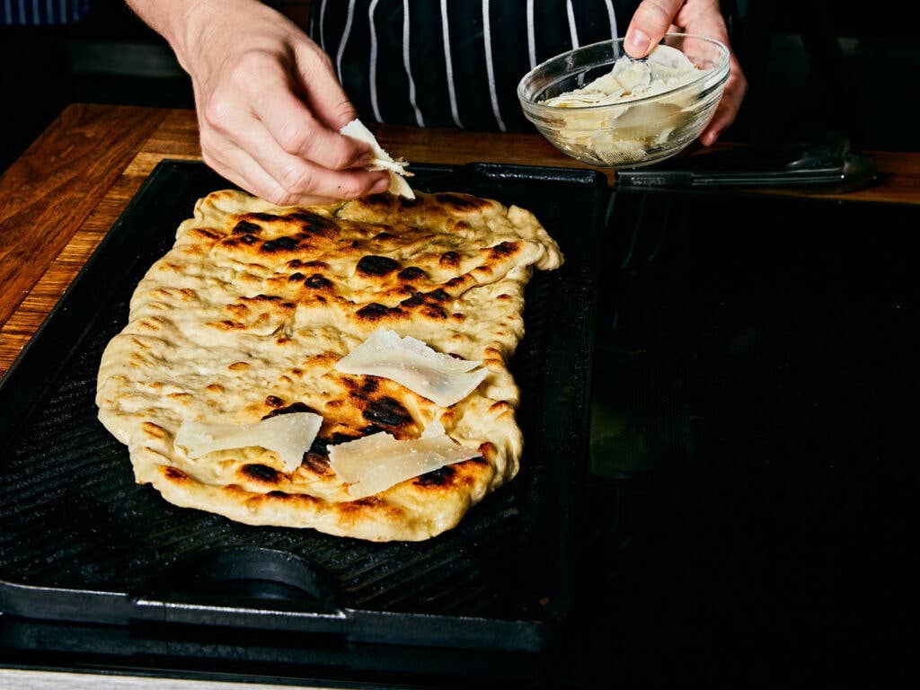 Thinly shaved parmesan cheese added to grilled pizza crust.