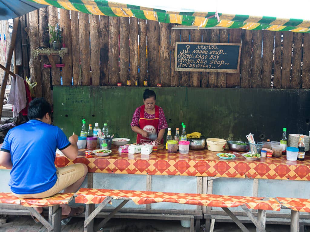 Man sits at vendor serving noodles in Laos.