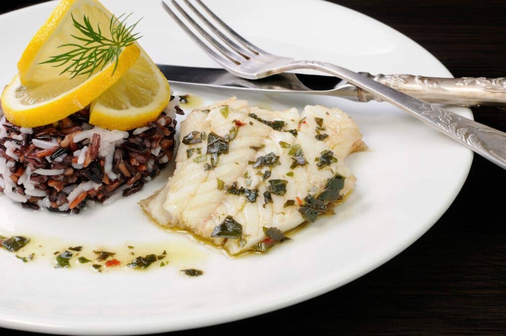 Slices of boiled fish with pesto and black, brown, and white rice on plate with silverware.