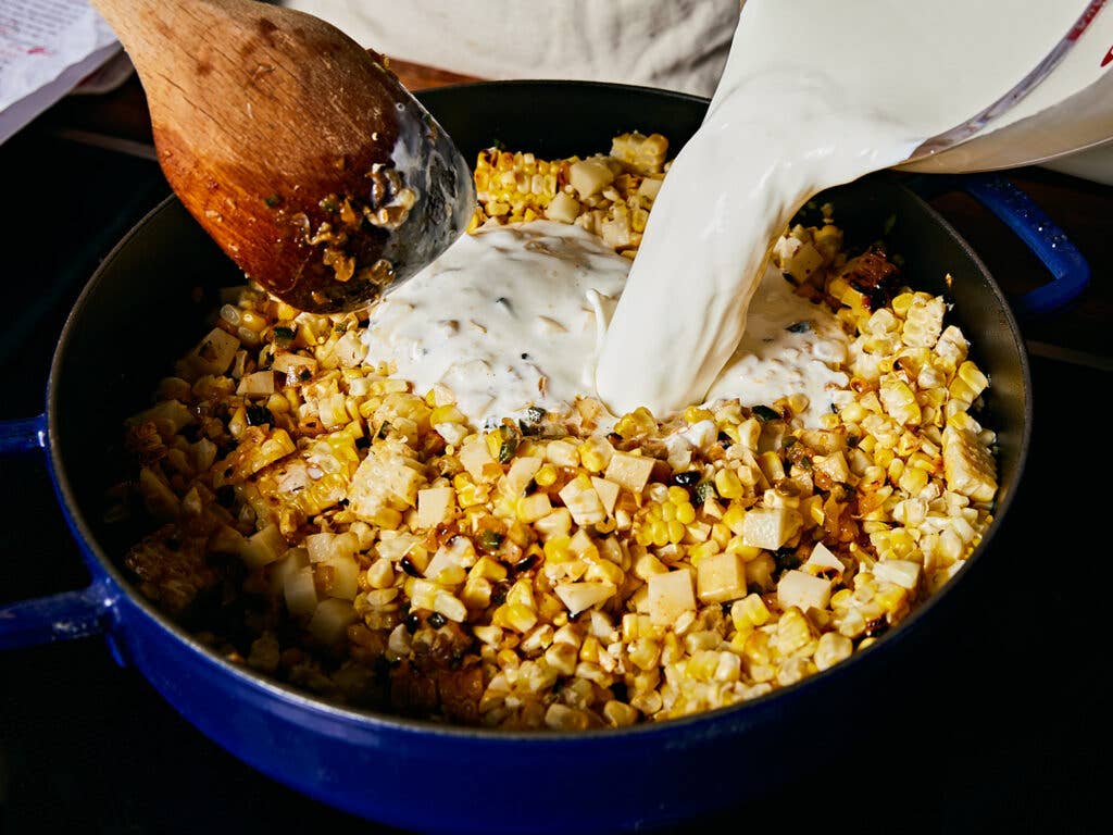 Pouring whole milk and heavy cream into grilled corn mixture.