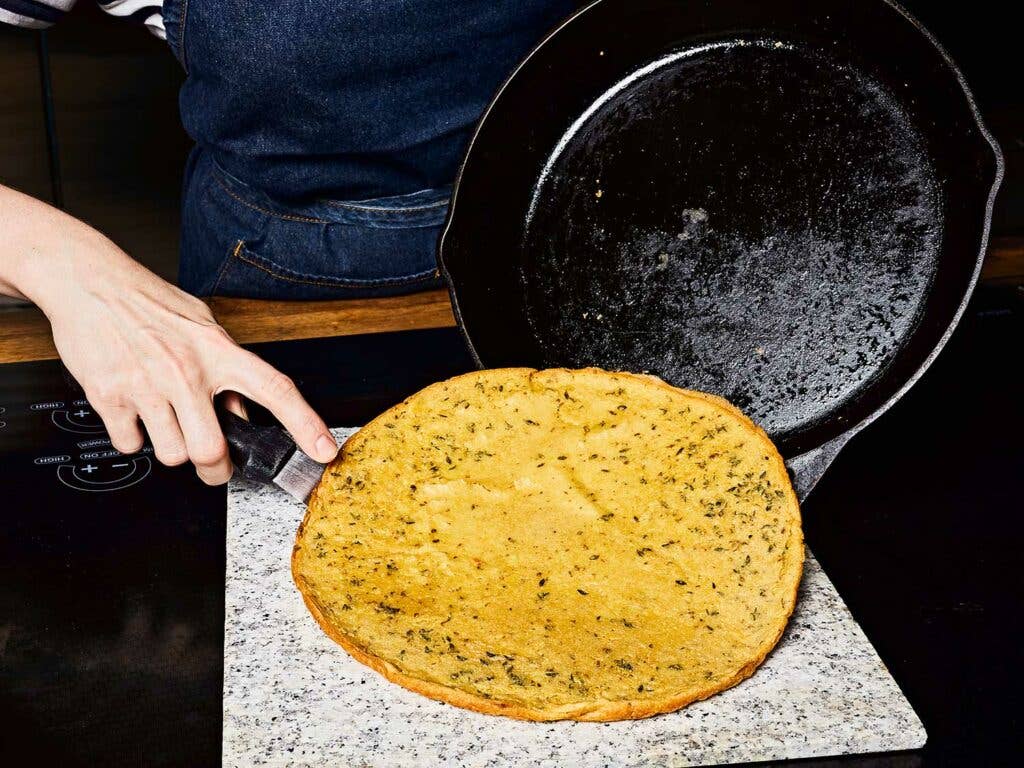 Using a thin offset spatula to remove the farinata from the skillet in one piece.