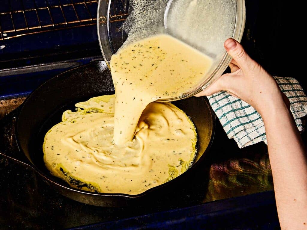 Pouring farinata batter into cast-iron skillet with olive oil.