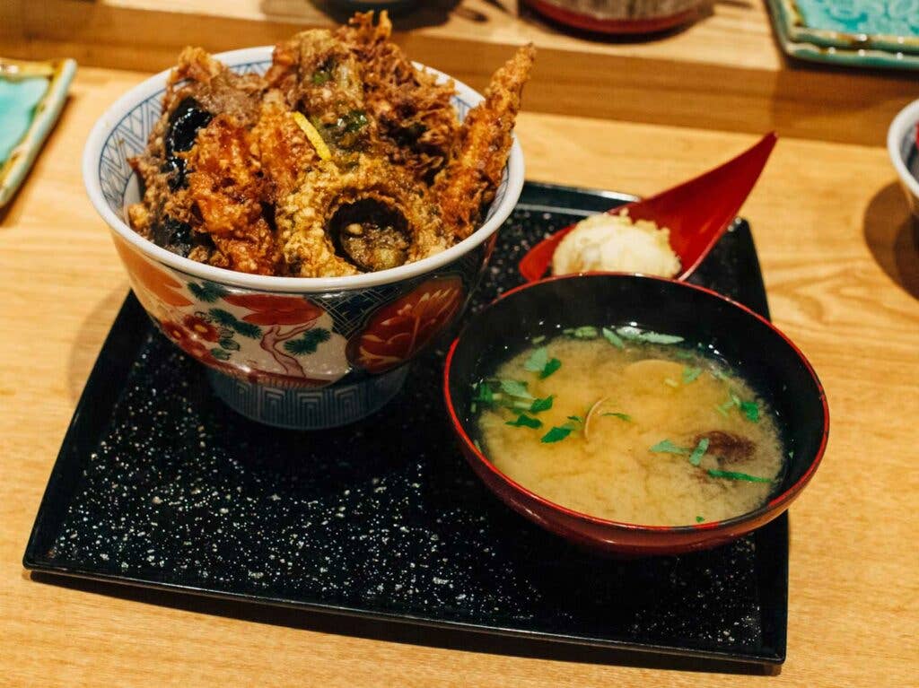 Isshin Kaneko’s summer tendon with eggplant, bitter melon, and baby corn, and is served with clam miso soup and soft-boiled egg tempura.