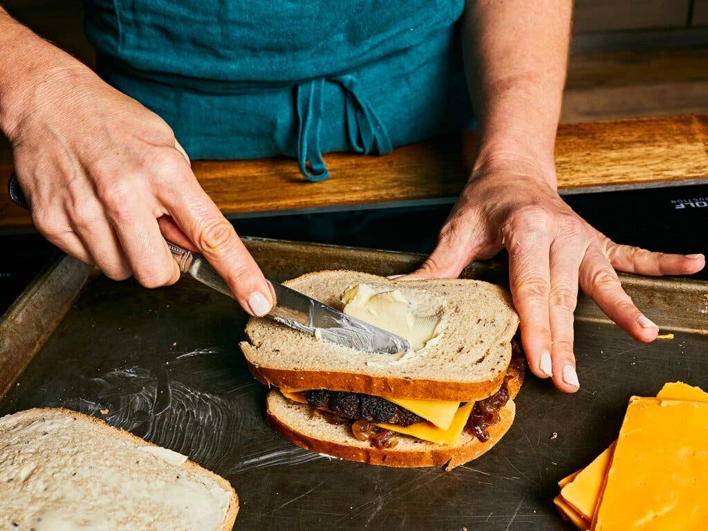 Buttering rye bread for patty melt on baking sheet.