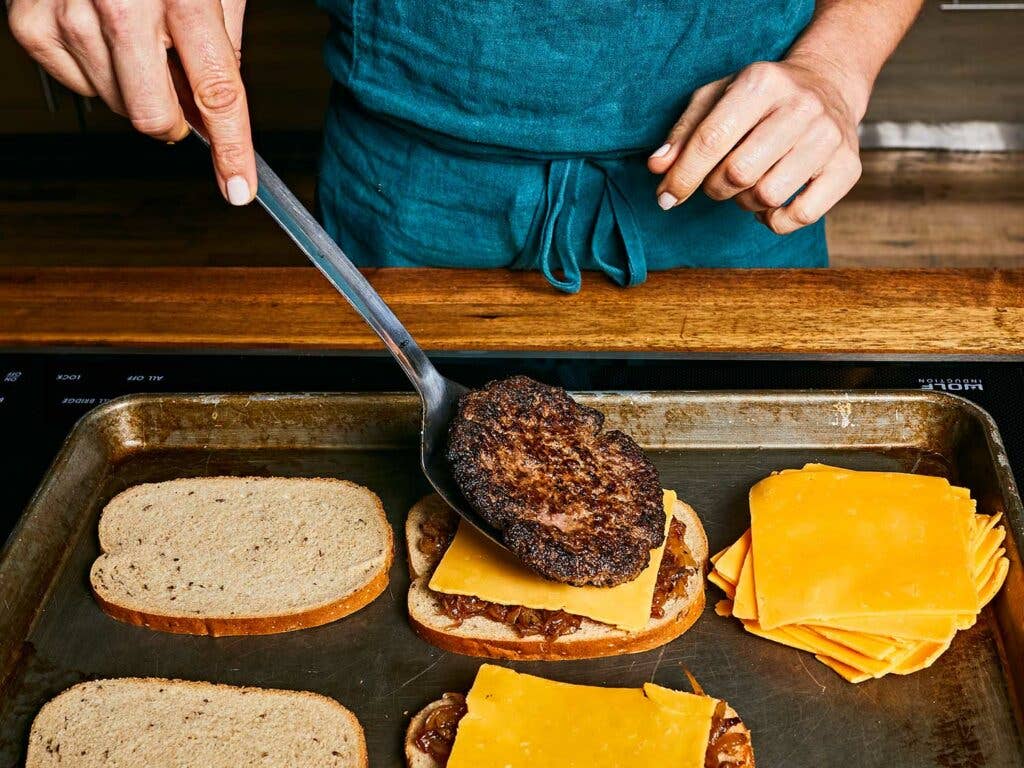 Adding warm patty on top, then topping with another layer of cheese.