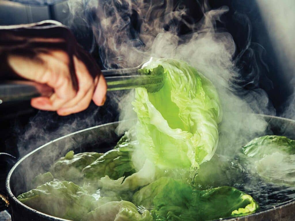 A cook parboils cabbage for rolls.