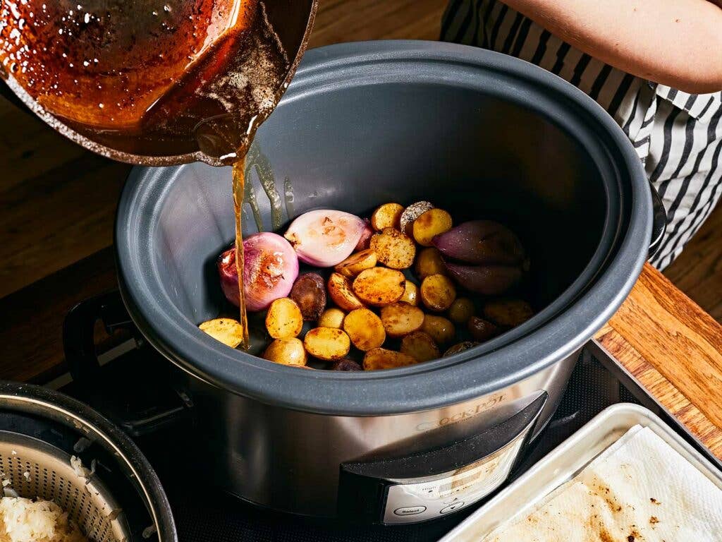 Pouring cooking fat over potatoes and shallots.