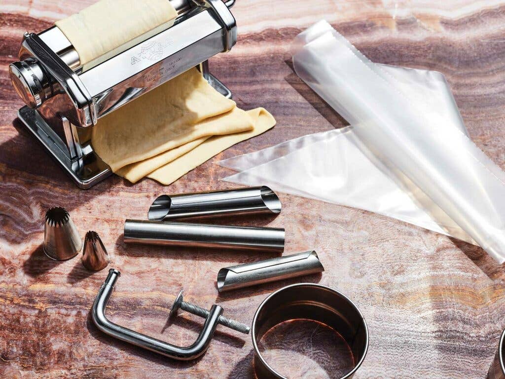 A pasta roller, piping tips, a ring cutter, and cannoli molds with rolled pastry.