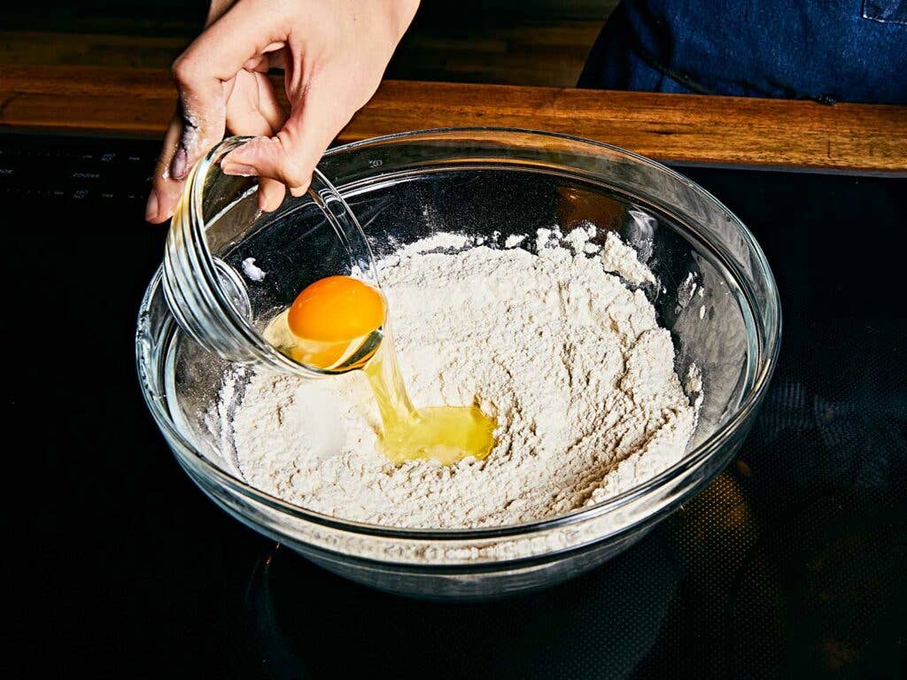 Adding an egg to the well in the dry ingredients.