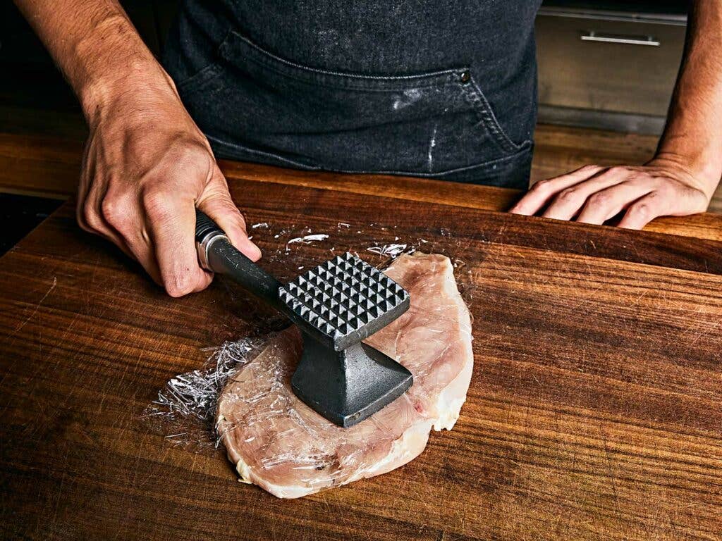 Pounding chicken breasts with meat mallet.