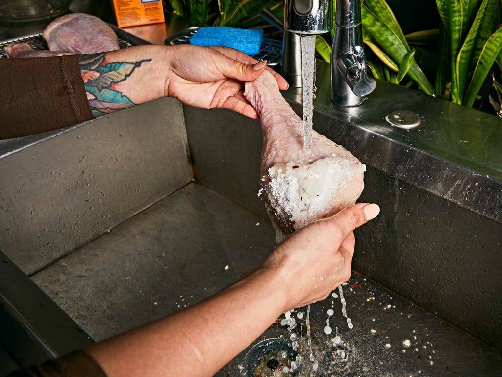 Rinsing turkey leg with cold running water to remove the dry brine.