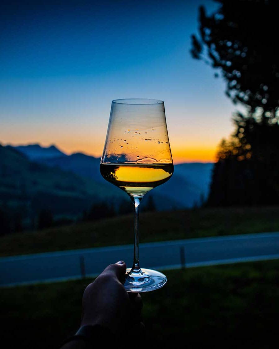 Glass of wine in front of sunset in mountains.