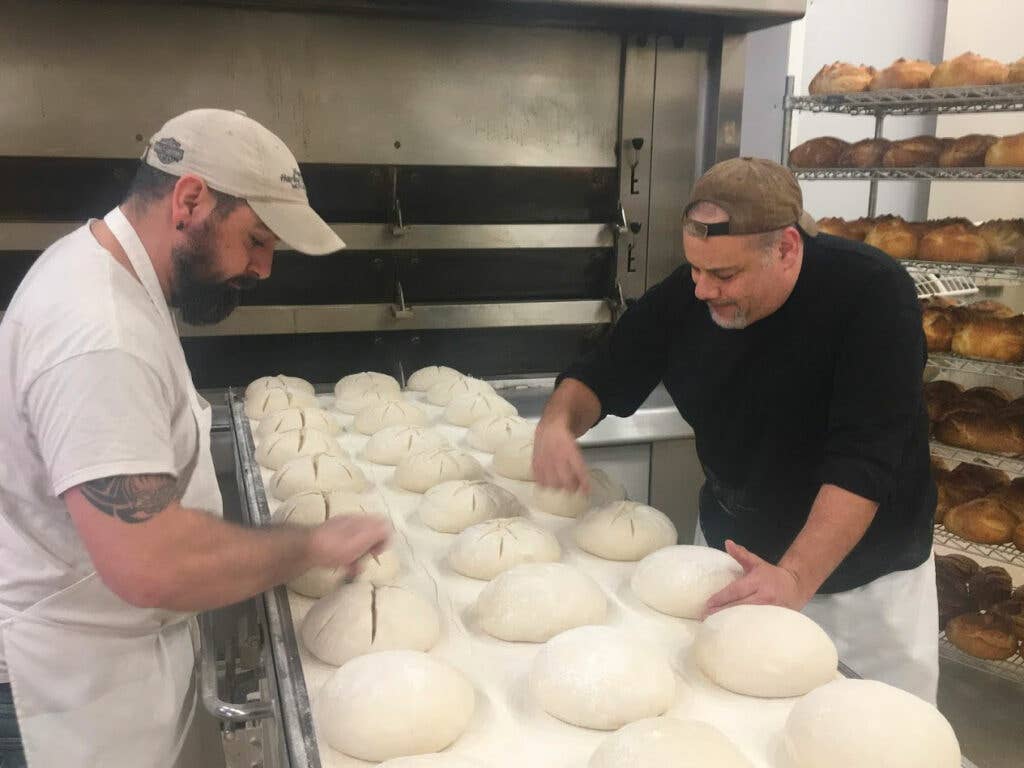 Matt Funiciello (right) scores hand-rolled boules before loading them into the deck oven at Rock Hill Bakehouse.