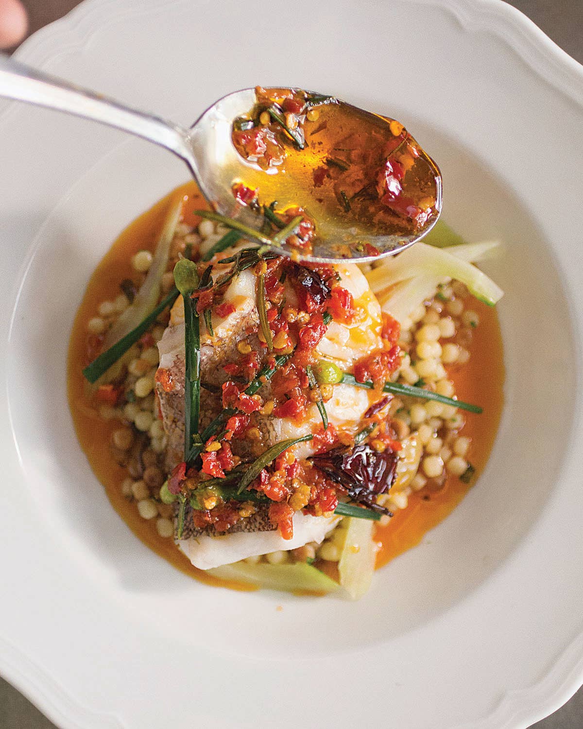 Calabrian chiles and chile paste produce a fiery, brick-red oil that is spooned over delicate steamed fish, crunchy spring vegetables, and fregola, a Sardinian pasta similar to Israeli couscous.