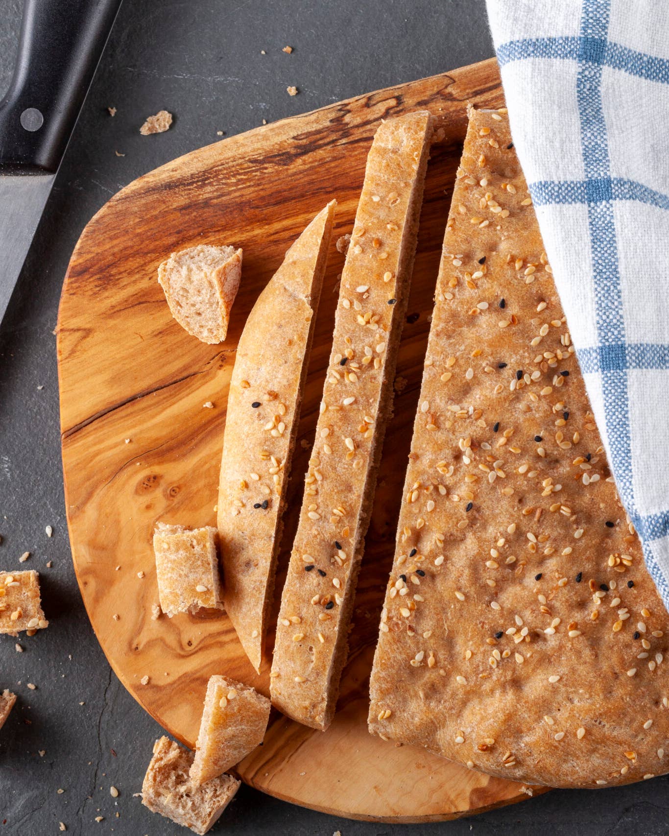 Flat lay image of Turkish Flat bread known as pide or pita on wooden chopping board. The wholegrain pita bread is round with poppy seeds and sesame seeds used as topping. It is diced and sliced