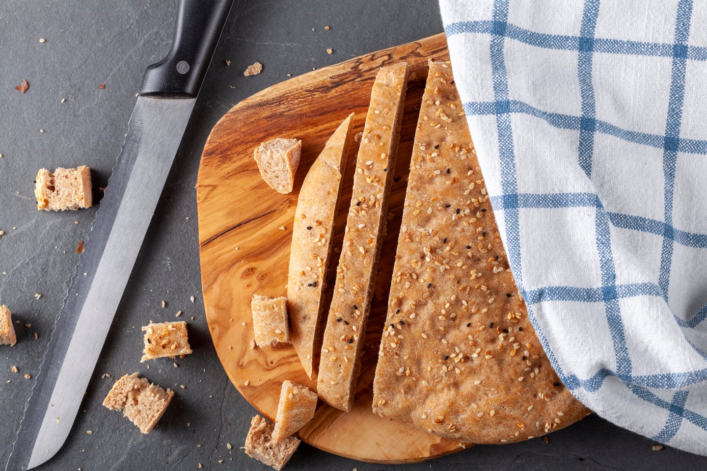 Flat lay image of Turkish Flat bread known as pide or pita on wooden chopping board. The wholegrain pita bread is round with poppy seeds and sesame seeds used as topping. It is diced and sliced
