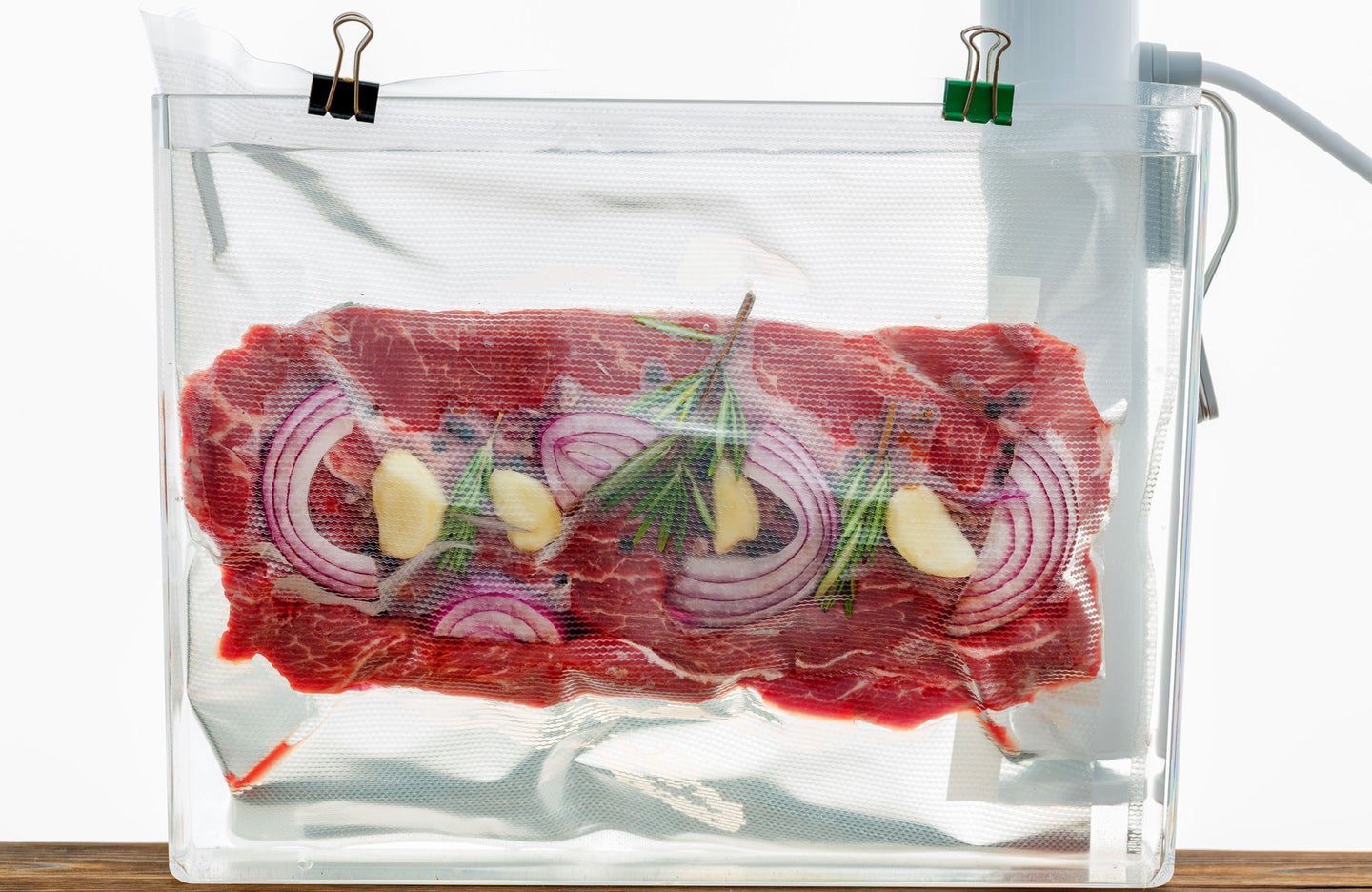 Sous vide bag containing raw beef, onions, and herbs