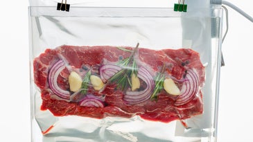 Sous vide bag containing raw beef, onions, and herbs