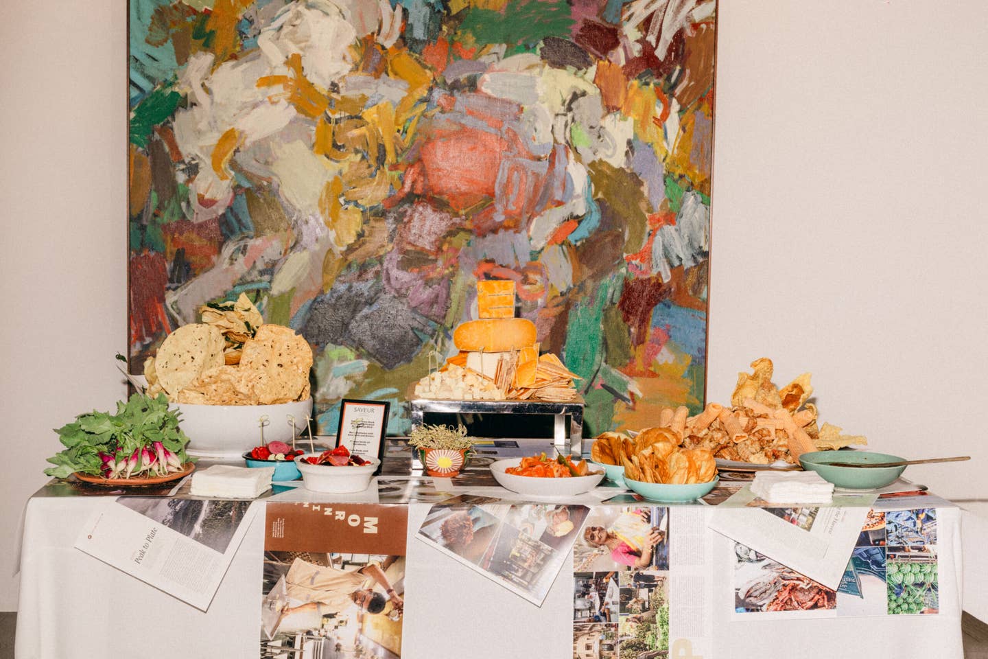 Puslapių pavyzdžiai iš naujausio numerio šefo Camille'o Becerra dailaus ganymo stalo, pastatyto priešais spalvingą Charleso Cajori paveikslą.