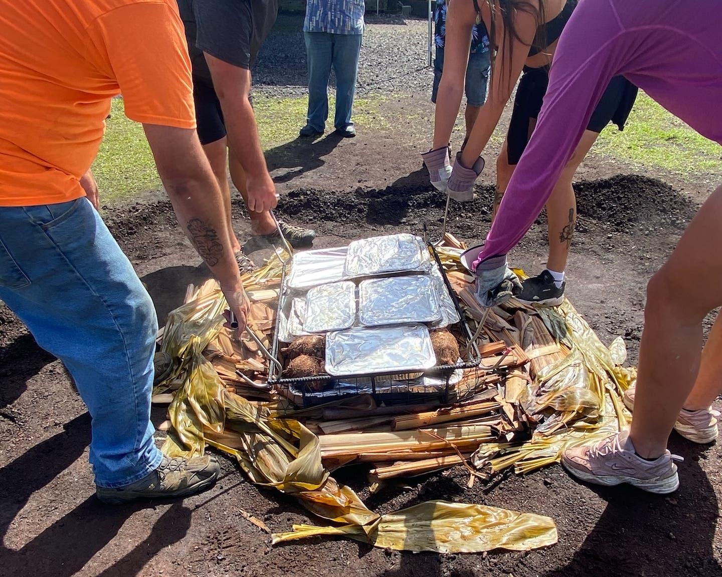 Volunteers lift hot trays of food to the imu.