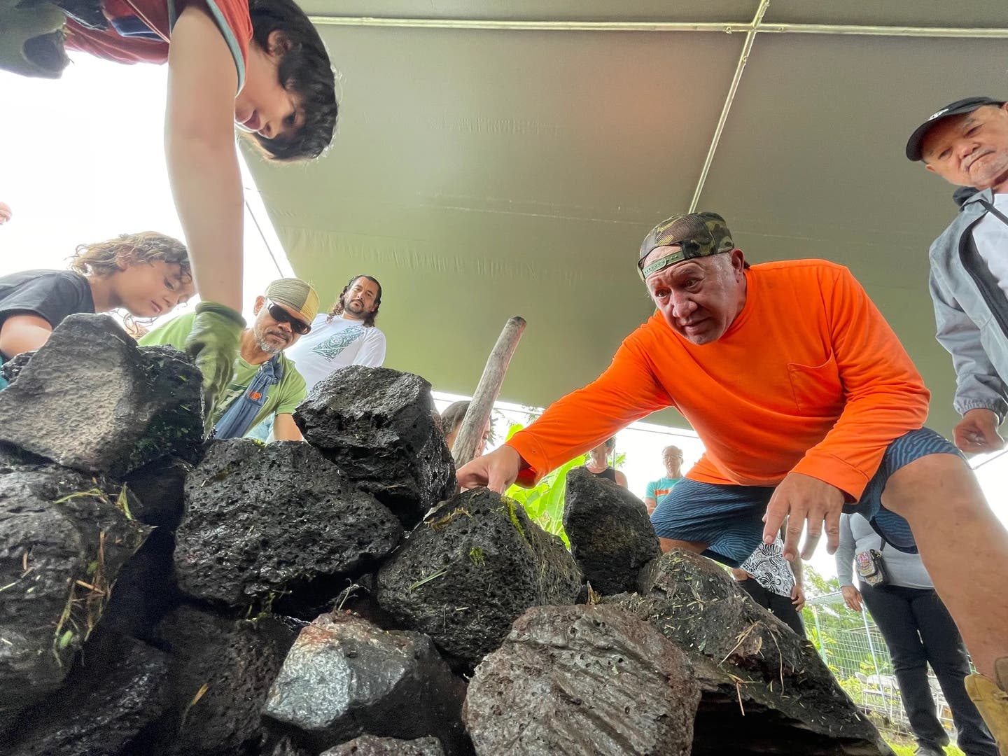 Iopa Maunakea instructs guests in stacking volcanic rocks to build an imu.